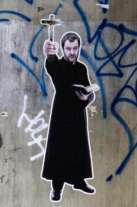 Un murales che ritrae il vicepremier e ministro dell'Interno Matteo Salvini in tonaca da prete, crocifisso brandito in una mano, libretto nell'altra, è apparso oggi a Roma in un sottopasso nel quartiere Ostiense. L'opera riporta sul bordo bianco che la circonda la scritta "Vattene, Satana, Vattene". Un riferimento alla copertina di Famiglia Cristiana - oggetto di forti polemiche - dove il ministro era rappresentato sotto il titolo 'Vade retro Salvini'. Sulle nocche del leader leghista compaiono inoltre le parole 'love' (mano destra) e 'hate' (sinistra), come quelle dell'inquietante predicatore interpretato da Robert Mitchum nel film 'La morte corre sul fiume', Roma, 28 luglio 2018. 
ANSA/ANGELO CARCONI